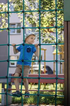 Little boy in blue t-shirt on an outdoor playground climbing green rope web.