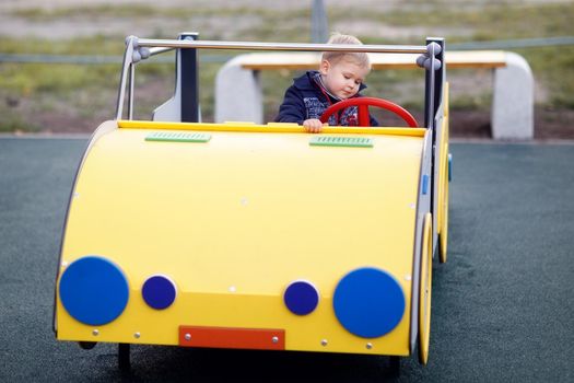 A little boy plays and drives a yellow big car on a playground. The child's interest and involvement in the play process