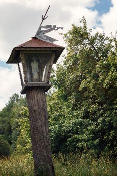 Lithuania, Plateliai, wooden carved chapel pillar with trumpet angel on top near the ethnographic homestead