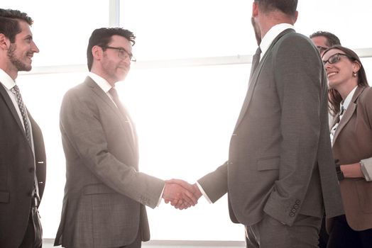 Business partners planning negotiation, exchanging contacts, thinking together about business development while standing near large window with modern urban landscape outside. Short meeting in office