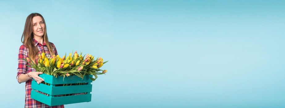 Happy caucasian young woman holding box with tulips on blue background.