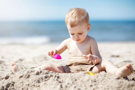 European two year old toddler boy playing with beach toys on beach. The child is very focused on wanting to create something out of sand