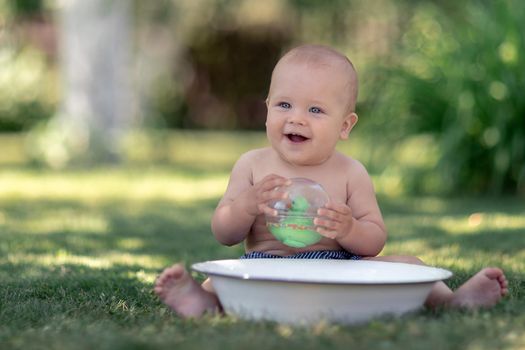 Cute baby hot summer day playing with a tub of water in the garden and smiling to the camera