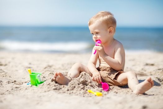 Little boy playing on the beach with sand beach toys. The boy is thinking about what to make of sand