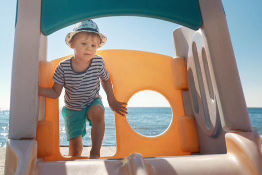 The boy climbs up to the orange children's slide on the beach