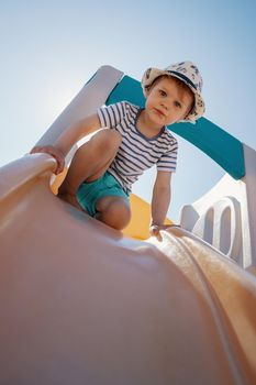 The little boy at the top of the slider prepares to slip and looks down