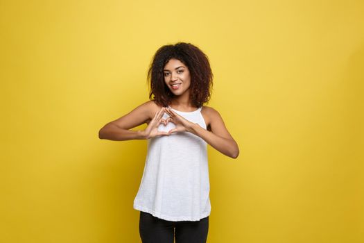 Isolated portrait of beautiful African American make heart symbol by hands. Yellow studio background. Copy Space