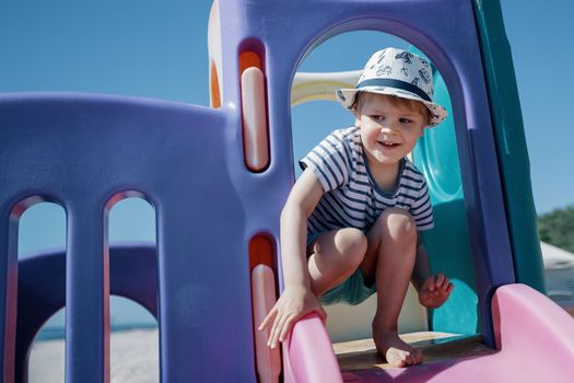 A little boy with a hat and a striped sailor shirt on the playground is ready to slide