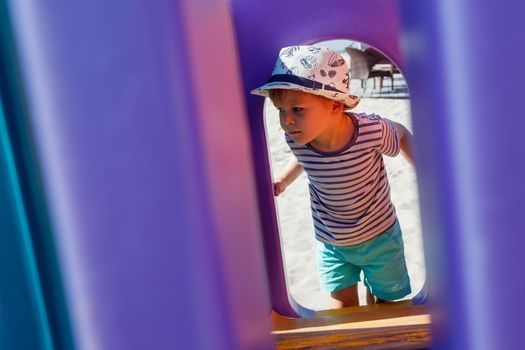 A little boy in a hat looks at the playground through a purple plastic arch. The purple background has free space for the note