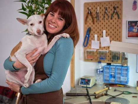 Portrait of an adult woman standing and holding her adorable dog in her workshop looking at camera.