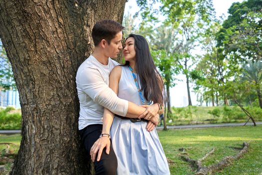 Profile of a multiracial couple about to kiss leaning against a tree in an urban park