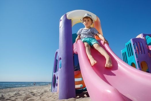 Colorful plastic slide on the beach background, cute little boy getting ready to slide down