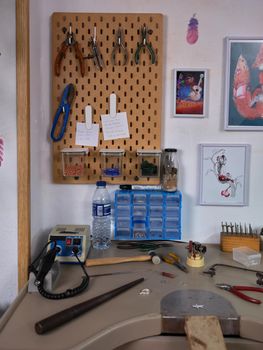 Vertical image of a workplace of an artisan jeweler in her workshop with various tools and the workbench.
