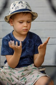 A little boy in a white hat looks at his hands, which he smeared when he drew with colored crayons