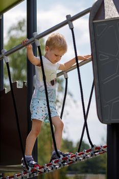 Low angle view of a little boy walking carefully across the playground monkey bridge.