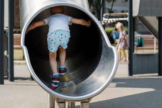 Young boy is having fun at the playground inside slide tube. Summer activity outdoors.