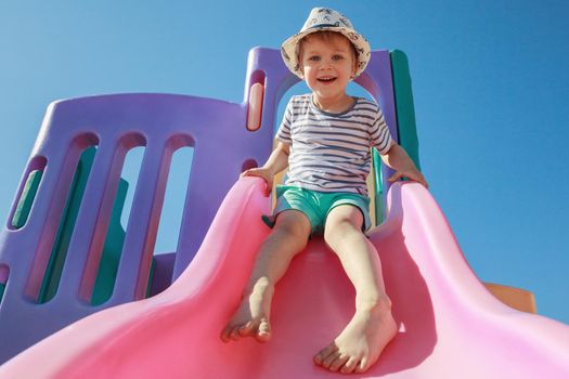 Cheerful little boy having fun while sliding outdoors, Happy toddler child on summer vacation