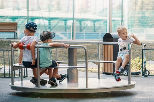 Group of happy kids having fun on roundabout at playground. Carousel for children in summer in the park.