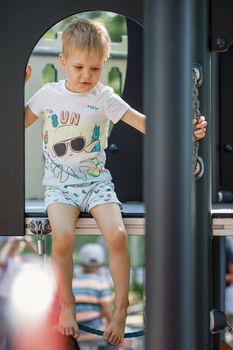 The little boy is playing on a modern playground. The child climbs dangerously high.