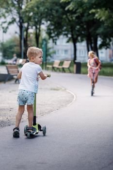 Child on kick scooter in park. A boy is riding on the kick scooter in a park. The concept of a healthy lifestyle. Kids sport.