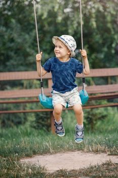 Little boy swinging high, smiling and looks to his mother. The child is very happy he likes to swing.