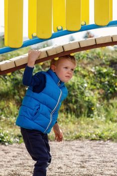 A little cute boy plays under a beautiful, curved bridge on a colorful playground. An agile child actively spends time in the fresh air. Vertical photo.