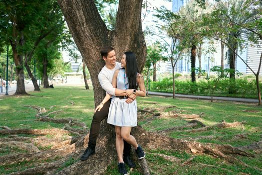 Photo with copy space of a multiethnic couple embracing while leaning against a tree in a park