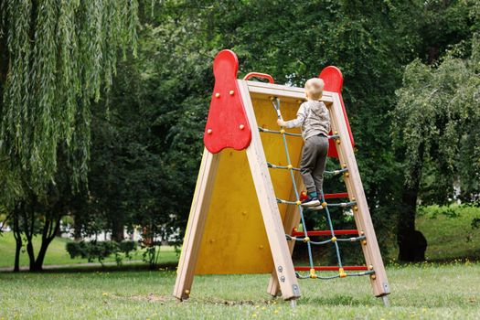 A child plays in a red rope web on the playground in the park.