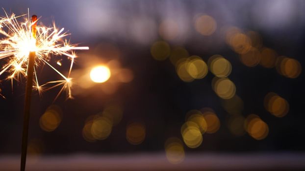 Sparkler firework burning on window, New Year or Christmas bengal lights. Winter Xmas holiday celebration magic, sparkles and golden fire stars light glowing in twilight of night. Garland in bokeh.
