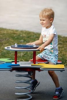 The cheerful boy springs up and balances on the swings of a modern outdoor playground.