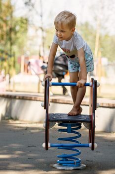 The brave little boy stands up and balances on a spring swing on the playground.