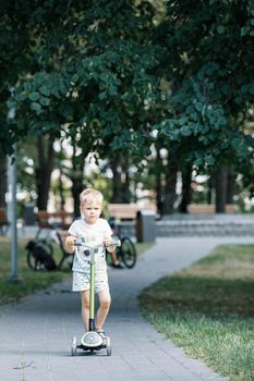 A little boy is riding a scooter in the park.