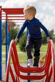 A little boy is climbing and hanging on a metal ladder in the form of an arc in the playground.