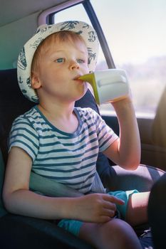 A little boy with a hat and a striped shirt trip to the beach he drinks juice from a plastic cup