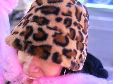 Close up view of a woman with a a leopard-textured hat biting a piece of cotton candy at night