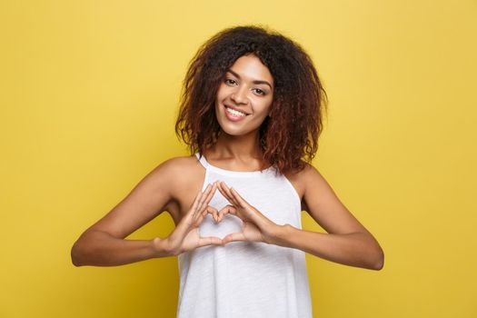 Isolated portrait of beautiful African American make heart symbol by hands. Yellow studio background. Copy Space