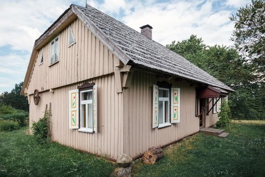 Old traditional wooden house with windows and shutters, rear view. An old carriage wheel is hung on the wall, the roof is covered with wooden tiles.