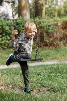 A little self-sufficient boy tries his best to climb a chain swing in a city park.