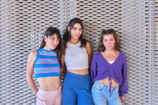 Three sensual young woman in vintage clothes posing while looking at the camera next to a urban wall