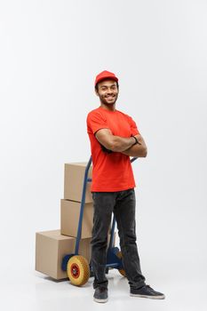 Delivery Concept - Portrait of Handsome African American delivery man or courier pushing hand truck with stack of boxes. Isolated on Grey studio Background. Copy Space