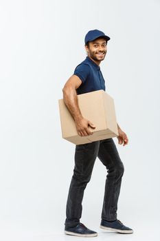 Delivery Concept - Portrait of Happy African American delivery man in blue cloth walking to send a box package to customer. Isolated on Grey studio Background. Copy Space