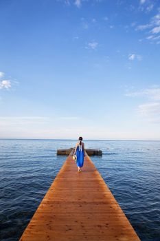 Montenegro, Budva. Girl in a blue dress stands on a wooden pier by the sea, beautiful sky with clouds. Vacation concept, travel to Europe