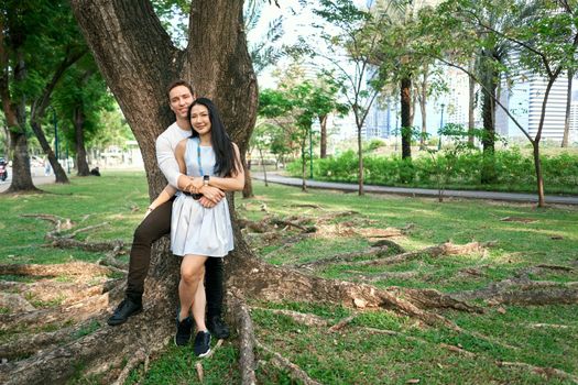 Photo with copy space of a newly married multicultural couple leaning on a tree in a urban park