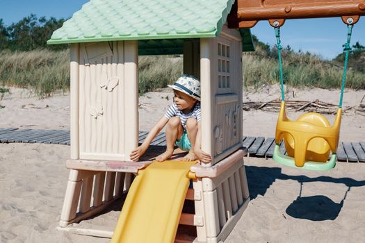 Children's playground on the beach, swings, slide, small hut and a cute child inside