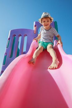 Happy kid playing slide at the playground under the sunlight in summer