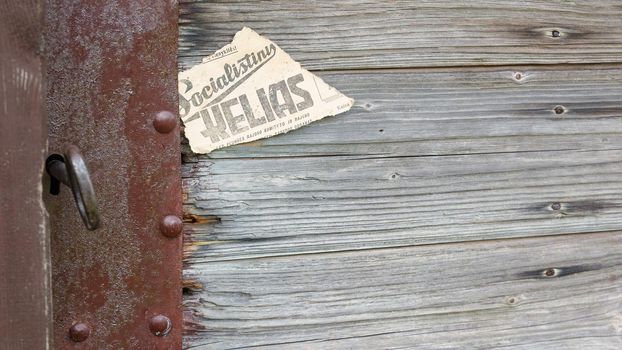 Lock, key, keyhole and piece of old newspaper on old wooden door. The old piece of the newspaper contains the inscription in Lithuanian language - "socialist path"