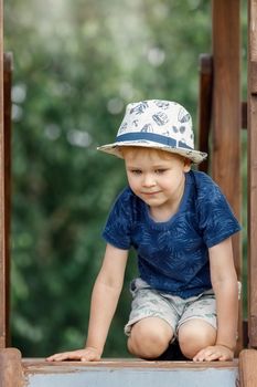 Portrait of a cute boy with a white hat and a blue shirt at the top of the playground.