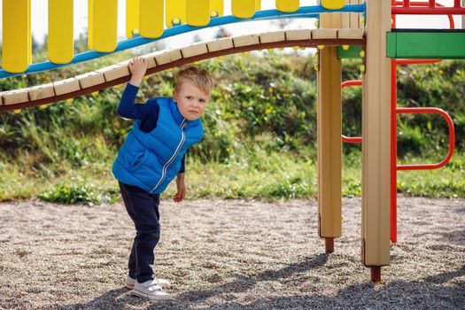 A little cute boy plays under a beautiful, curved bridge on a colorful playground. Horizontal photo.