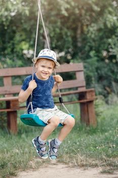 Portrait of little boy playing on swing in grandmother's garden.