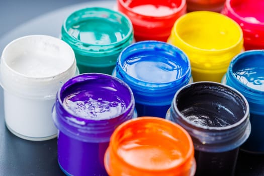full-frame close-up background of opened small gouache paint jars on black